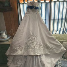 a wedding dress hanging on a rack in front of a window with blue and white striped curtains