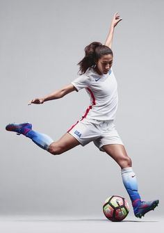 a woman is kicking a soccer ball on a gray background with her legs spread out