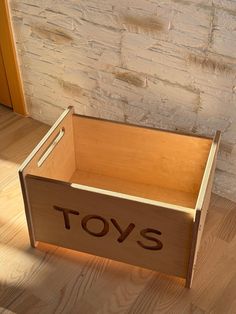 a wooden toy box with the word toys on it sitting in front of a brick wall