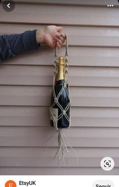 someone is holding a bottle of wine in a rope hanging from the side of a house