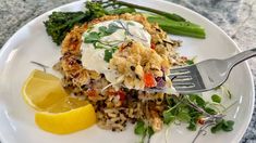 a white plate topped with rice covered in sauce next to asparagus and lemon wedges