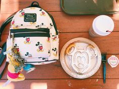 a mickey mouse backpack sitting on top of a wooden table next to a plate with donuts