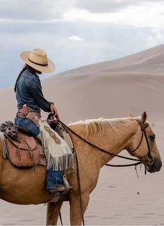 a man in cowboy attire riding a horse through the desert with sand dunes behind him