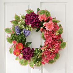 a wreath is hanging on the front door with flowers in blooming around it and green leaves