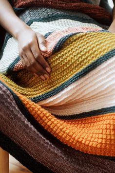 a woman sitting on a chair holding a multicolored blanket over her stomach and hand