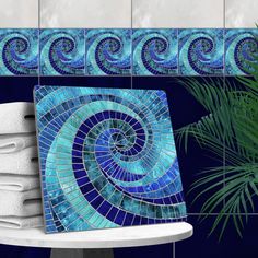 a blue mosaic tile design on a wall next to a stack of towels and a potted plant