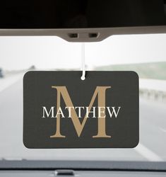 a black and gold monogrammed car tag with the letter m hanging from it