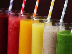 five different colored smoothies lined up in glass cups with straws on each side