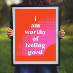 a woman holding up a framed poster with the words i am worthy of feeling good