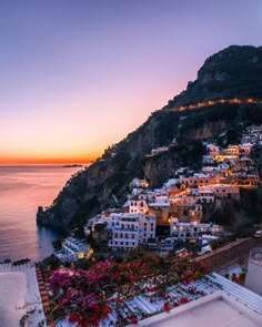 the sun is setting over an ocean and some buildings with flowers in front of them