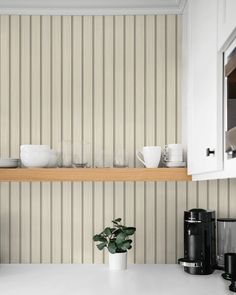 a kitchen counter with plates and cups on it, next to a coffee maker in front of a striped wall