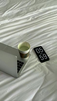 a laptop computer sitting on top of a white bed next to a cup of coffee