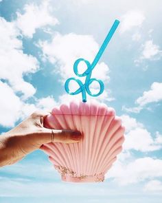 a hand holding a pink shell with blue scissors sticking out of it's top