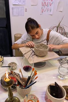 a woman sitting at a table working on a clay sculpture with candles in the background