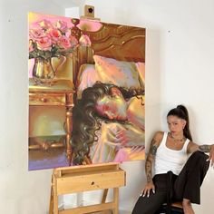 a woman sitting on a chair in front of a painting with flowers and a vase