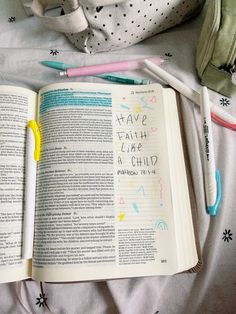 an open book sitting on top of a bed next to a stuffed animal and pencils