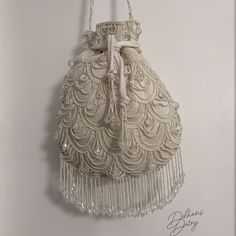 Step into a world of timeless elegance with our exquisite handmade ivory beaded bridal potli bag. Crafted with meticulous attention to detail, this enchanting accessory seamlessly blends tradition with modernity. Each delicate bead has been carefully chosen and skillfully hand-sewn. The potli bag's intricate beadwork showcases a stunning fusion of classic design and contemporary flair, making it a perfect match for brides seeking a touch of refined charm. The bag's compact size and comfortable h Luxury Beige Shoulder Bag For Wedding, Beige Beaded Bags For Reception, White Embroidered Potli Bag For Evening, Elegant Beaded Pouch Potli Bag, Elegant Beaded Potli Bag, White Beaded Bag For Reception, Handmade Cream Bags For Formal Occasions, White Bags With Pearl Handle For Reception, Beige Bags With Pearl Embroidery For Reception