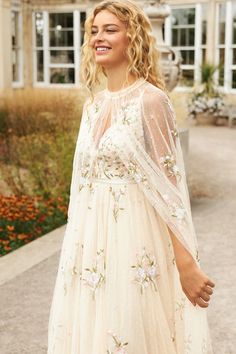 a woman wearing a white dress with flowers on it and a veil over her head