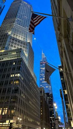 an american flag is flying in the sky above some tall buildings at night with lights on