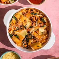 two bowls filled with pasta and sauce on top of a pink tablecloth next to other dishes