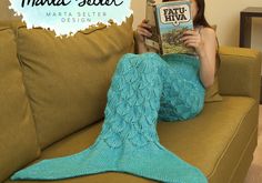 a woman sitting on a couch reading a book with a knitted mermaid tail blanket