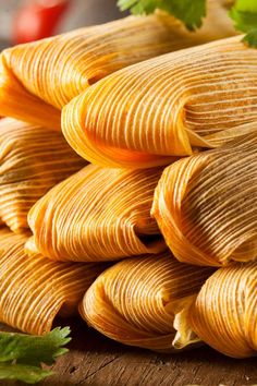 several tamales stacked on top of each other with parsley next to them and tomatoes in the background