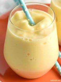 two glasses filled with yellow liquid on top of an orange plate next to blue and white straws