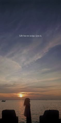 a woman is standing on the beach watching the sun go down and there is a boat in the distance