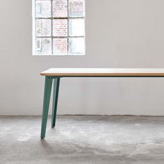 a wooden table with two green legs in front of a white brick wall and window