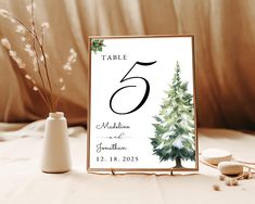 a table number sign with a christmas tree on it and two vases next to it