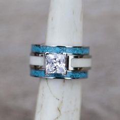 a white and blue ring with a princess cut diamond in the center on a marble pedestal