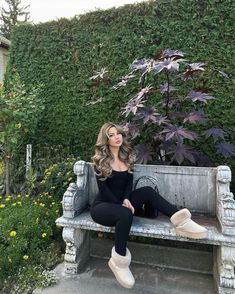 a woman sitting on top of a bench next to a lush green wall