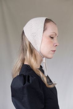 a woman with blonde hair wearing a white knitted headband and black shirt, looking down