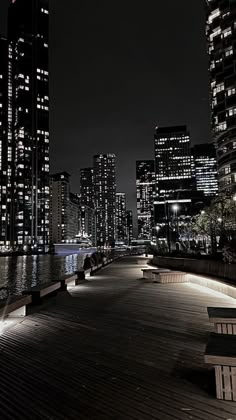 the city skyline is lit up at night, with benches along the water's edge