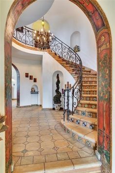 an arched doorway leading to a staircase with wrought iron railing and hand painted tiles on the floor