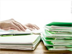 a person typing on a computer keyboard next to stacks of folders and papers with their hands