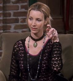 a woman sitting on top of a brown couch wearing a black shirt and beaded necklace