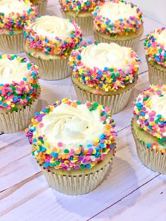 cupcakes with white frosting and sprinkles on a wooden table