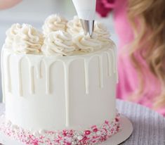 a white cake with icing and sprinkles is being cut by a woman