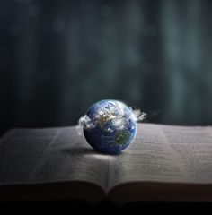 an open book with the earth on top and clouds coming out of it's pages