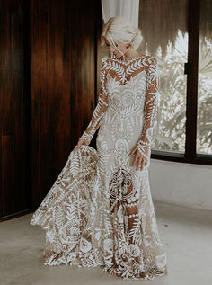 a woman in a white wedding dress with long sleeves and an intricate lace pattern on it