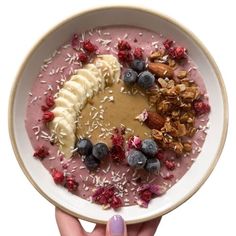 a person holding a bowl of oatmeal with bananas, blueberries and granola