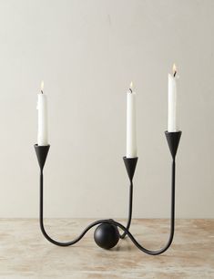 three white candles sitting on top of a wooden table next to a black candle holder