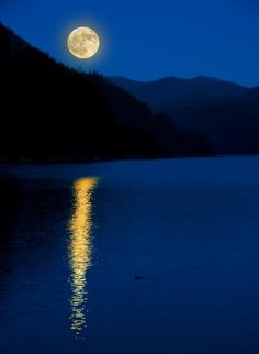 the full moon is shining brightly in the night sky over a body of water with mountains behind it