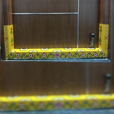 a yellow and green window frame with decorative designs on the outside, in front of a wooden wall