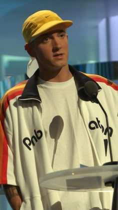 a man with a yellow hat standing at a podium in front of microphones and talking