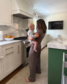 a woman holding a baby while standing in a kitchen