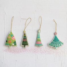 three christmas trees hanging from strings on a white wall with pink and green sprinkles