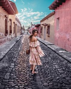 a woman walking down a cobblestone street in an old town with pink buildings