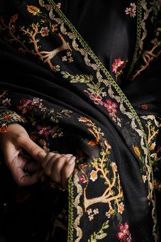 a close up of a person wearing a black and gold embroidered dress with flowers on it